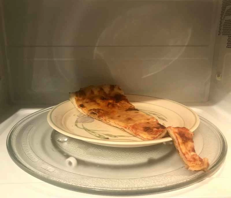 先把一片起司披薩放進微波爐加熱，再放進烤箱。這不是加熱披薩的最佳方法，但勉強夠用。