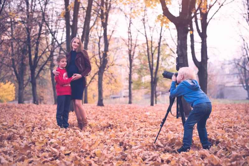 一個金髮小男孩，手裡拿著一台架在三腳架上的單眼相機。