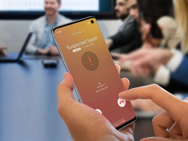 一個人坐在會議室裡，手裡拿著一部三星手機，手機上的「智慧通話」應用程式正在提醒他有騷擾電話。