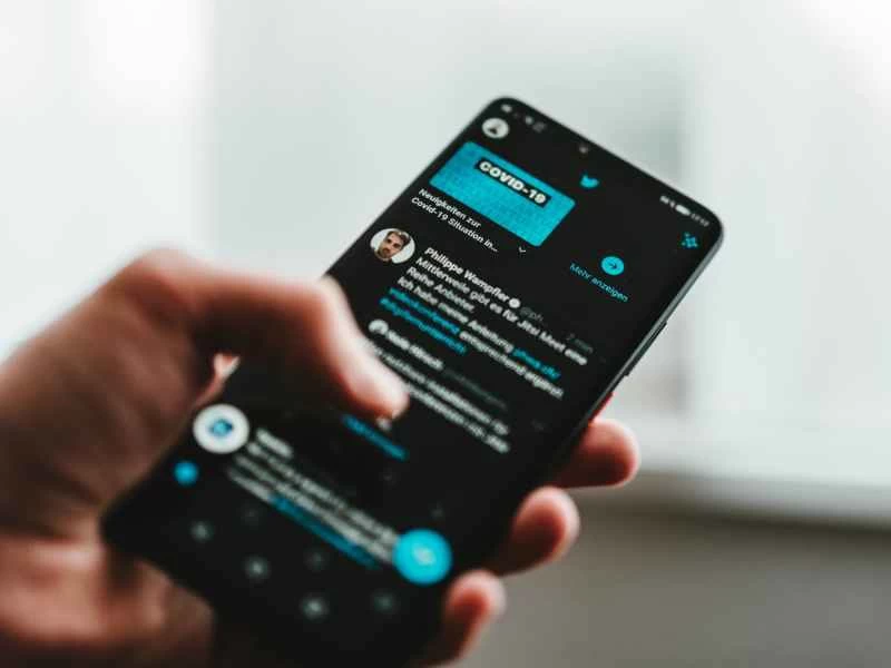 一個人拿著手機，在深色模式下使用 Twitter，瀏覽有關 COVID-19 的推文。