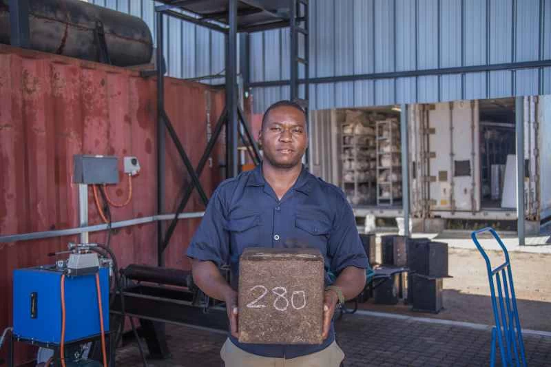 倉庫裡，一名身穿藍色襯衫的男子手持壓縮菌絲體。