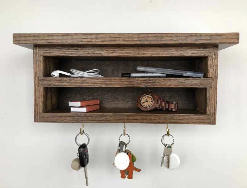一個小型橡木層架鑰匙收納櫃，用法式掛鉤懸掛在牆上，看起來像是懸浮在牆上一樣。
