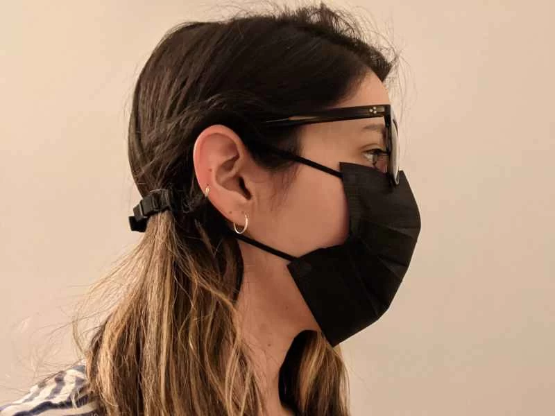 一位金髮女子戴著黑色口罩，口罩上加裝了口罩延長器，同時戴著眼鏡，以防止鏡片起霧。