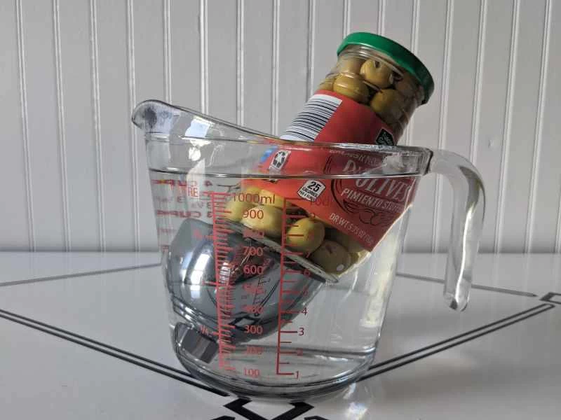 量杯中盛有水和檸檬酸的混合物，用於清潔淋浴噴頭——淋浴噴頭被一罐橄欖壓住。