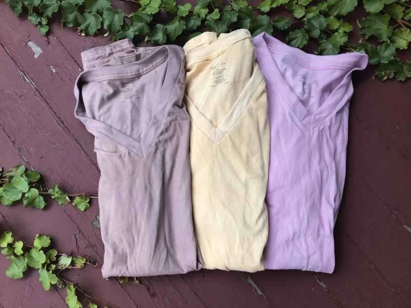 木質階梯上擺放著三件自製染色襯衫。由左至右依序為：灰色、黃色和粉紅色。