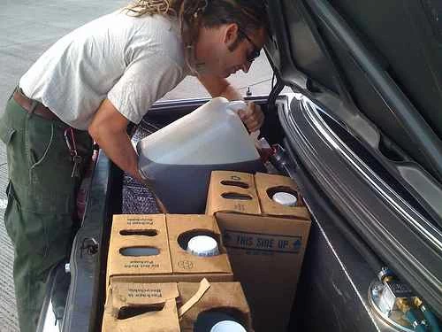 一名身穿白色T恤和綠色褲子的男子正在將植物油倒入一輛改裝過的、以植物油為燃料的賓士車的油箱中。