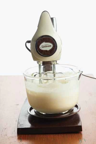 一台Sunbeam牌立式攪拌機正在攪拌一碗蛋糕糊。