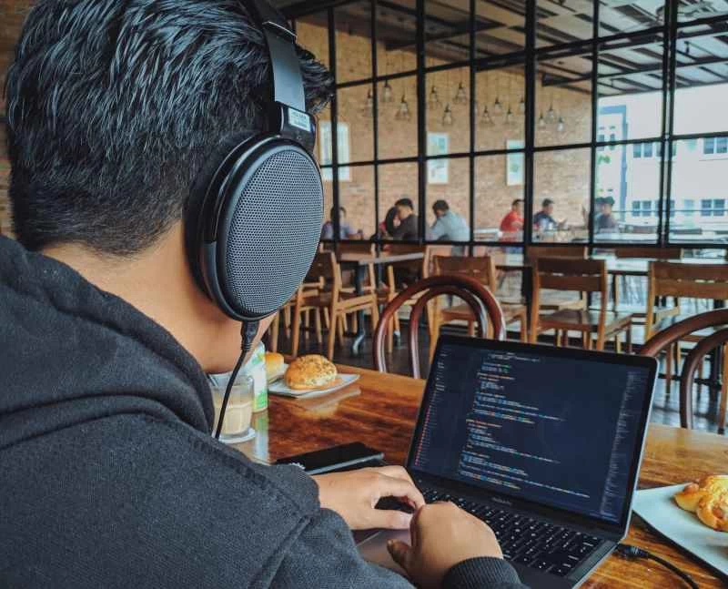 一名男子戴著耳機，在咖啡館使用筆記型電腦工作。