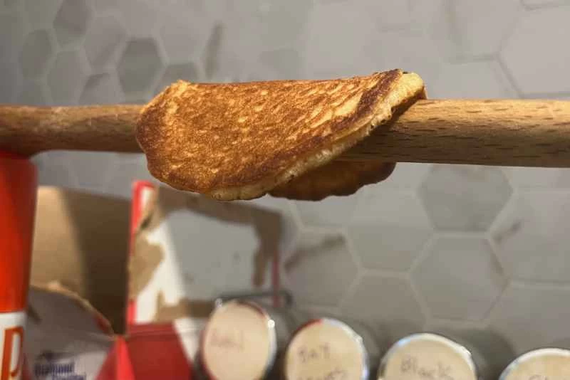 一個華夫餅筒，或者說華夫餅煎餅，搭在一根木湯匙上，木湯匙被拉緊在兩個容器之間。